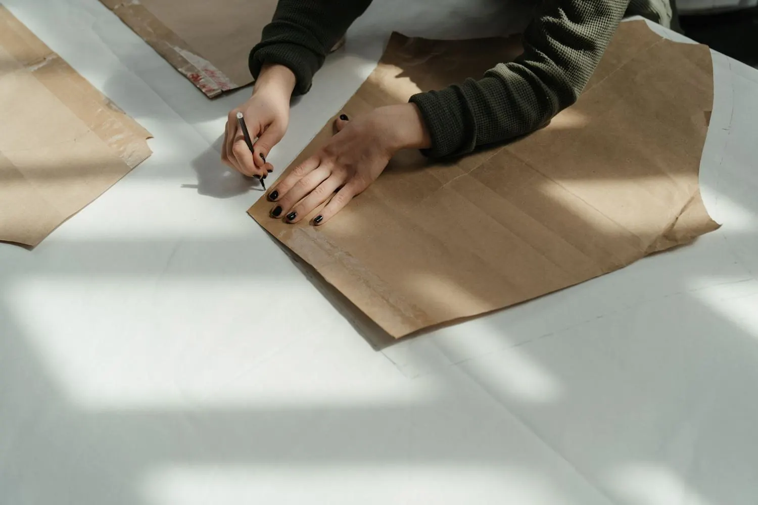 Mãos a riscar um molde de papel sobre uma mesa de corte